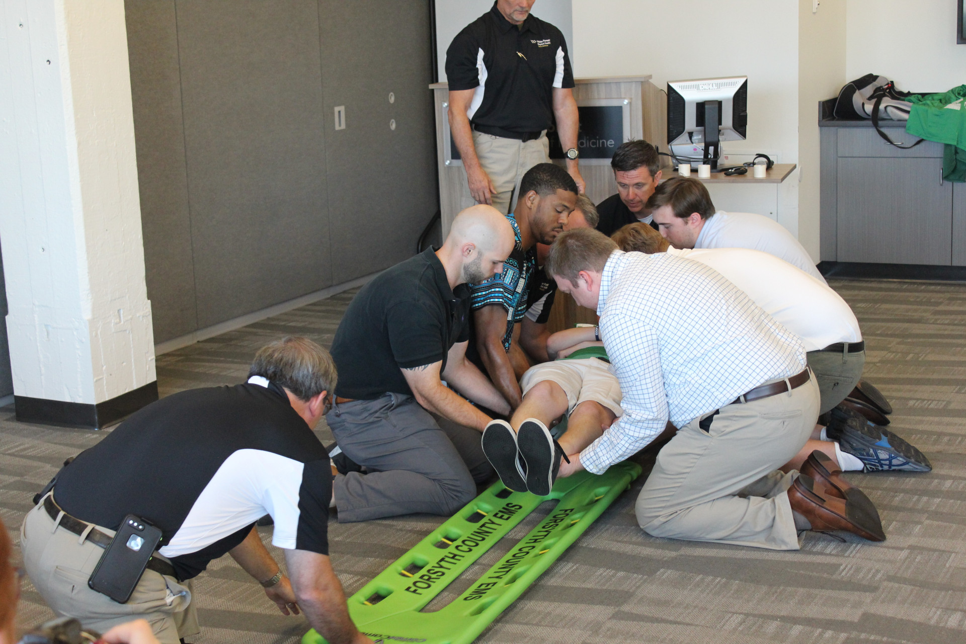 Wake Forest athletic trainer Chris Ina (kneeling, top of spine board) and EMT Jeff Hinshaw (kneeling, bottom of spine board) demonstrate proper technique to placing a spine board under an athlete with a potential spine injury (Daniel Coston Photo)